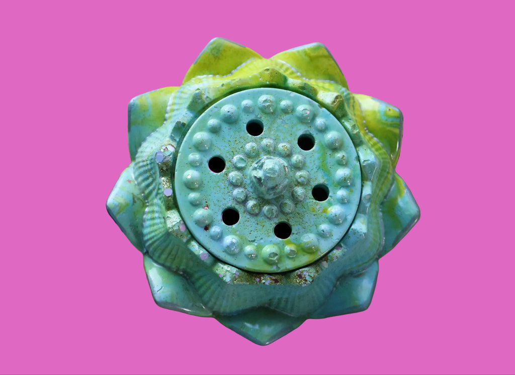 Decorative turquoise and green cement item on a wooden surface with a floral fabric background.