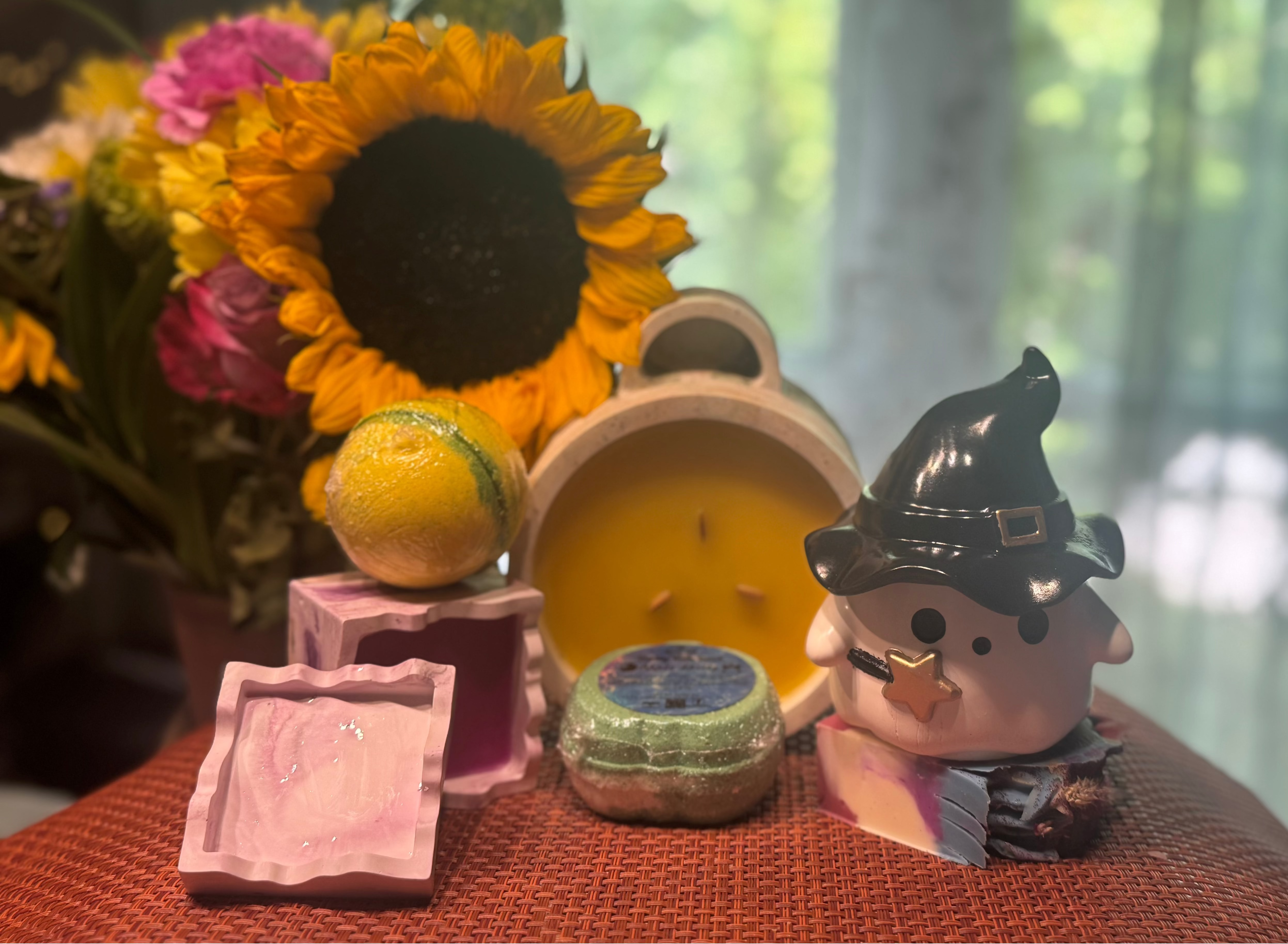 Decorative items including a sunflower, candles, and a small figurine on a table with a blurred natural background.